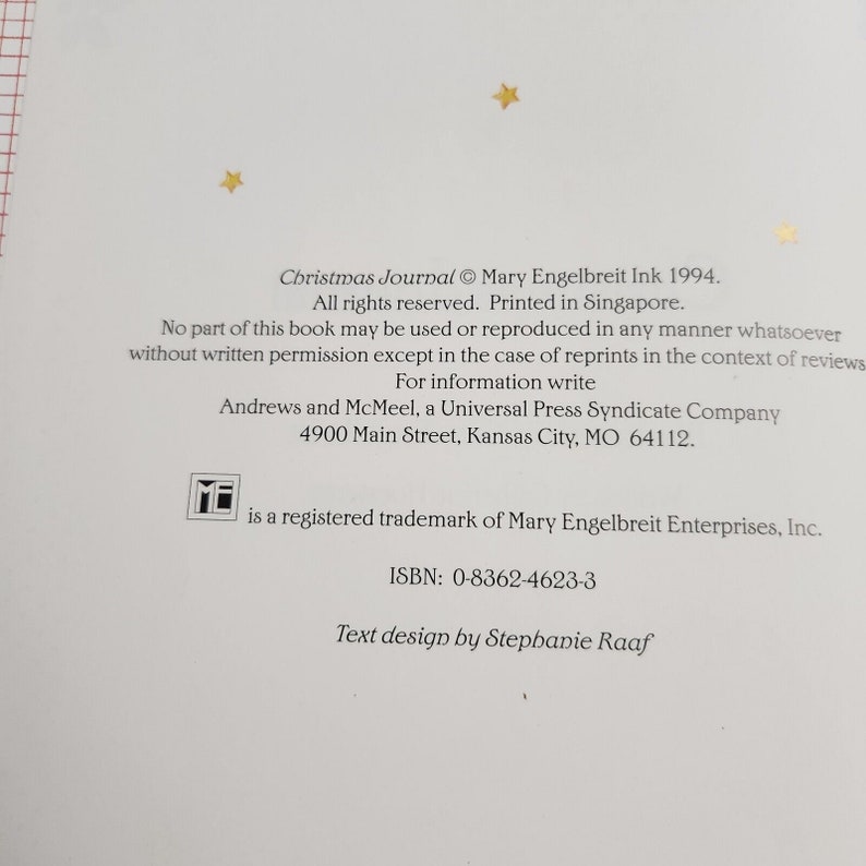 May include: A book cover with a white background and gold stars. The title "Christmas Journal" is printed in black text. The book was published in 1994 by Mary Engelbreit Ink. The copyright information includes the text "All rights reserved. Printed in Singapore."