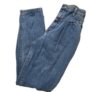 May include: High-waisted blue denim jeans featuring a pleated front design, a button and zip fly closure, belt loops, and a tapered leg silhouette. The fabric has a medium wash finish with visible stitching along the seams and pockets.