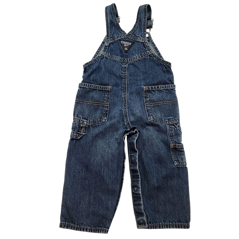 May include: Dark blue denim overalls with multiple pockets, including two front pockets, two back pockets, and a small bib pocket. The overalls have adjustable straps and button closures. The brand name "OshKosh B'gosh" is visible on the bib.