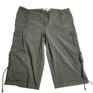 May include: Olive green cargo shorts with multiple pockets and drawstring details. These knee-length shorts feature a button and zipper closure, offering a casual and practical style. The shorts are made of a durable fabric.