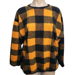 May include: A black and orange plaid sweater with a crew neck. The sweater has long sleeves and a loose fit. The plaid pattern is made up of large squares of black and orange. The sweater is made of a soft, fuzzy material.