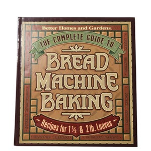 May include: A hardcover book titled Better Homes and Gardens The Complete Guide to Bread Machine Baking. The cover features a brown and tan grid background with green and red banners. It includes text for 1 1/2 & 2 lb. Loaves.
