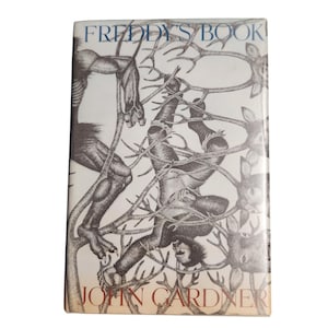 Op de afbeelding: Een vintage boek getiteld "Freddy's Book" van John Gardner. De omslag toont een zwart-wit illustratie van figuren verstrikt in takken. Het boek heeft een witte achtergrond met blauwe en rode tekst.