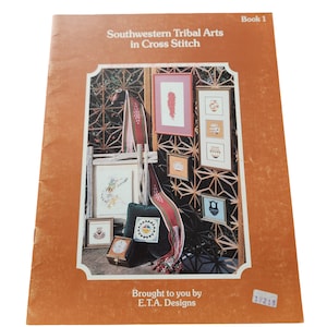 Puede incluir: Un libro vintage titulado "Southwestern Tribal Arts in Cross Stitch" con una portada marrón. La portada presenta arte de punto de cruz enmarcados, incluyendo un chile rojo y diseños geométricos. También es visible el texto "Brought to you by E.T.A. Designs".