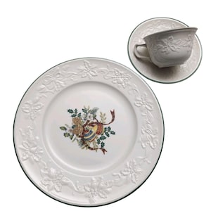以下が含まれることがあります： 白磁のティーカップとソーサーのセットと、お揃いのディナープレート。セットは、縁に沿って浮き彫りの花の模様と、お祝いのオーナメントと緑の葉のモチーフが特徴です。プレートには緑色のトリムが付いています。