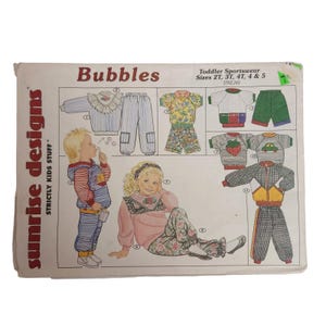 May include: A vintage sewing pattern labelled "Bubbles" by Sunrise Designs. The pattern shows illustrations of toddler sportswear in sizes 2T, 3T, 4T, 4 & 5. The designs include tops, trousers, and a jacket with various patterns and details.