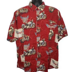 Puede incluir: Camisa roja de manga corta con estampado de motocicletas y banderas americanas. La camisa presenta un diseño repetido de motocicletas, águilas y banderas. Tiene un cuello clásico y cierre de botones.