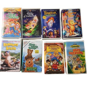 May include: A collection of eight VHS tapes featuring animated movies. Titles include "Tom Sawyer," "Troll in Central Park," "Bartok the Magnificent," and "The Tangerine Bear." Other titles are "Runaway Ralph," "Brother Bear," "An American Tail," and "The Ugly Duckling."