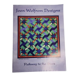 Op de afbeelding: Een patroonboekje van Joen Wolfrom Designs getiteld Pathway to the Stars. De omslag toont een quilt met een geometrisch ster- en windmolenpatroon in tinten blauw, groen en oranje, tegen een lichtblauwe achtergrond met tekst.