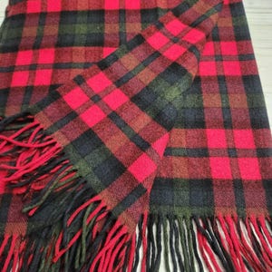 May include: A red, black, and green tartan scarf with red fringing. The scarf is folded, displaying the pattern of the fabric. The tartan pattern is a classic design, with thick lines and bold colours.