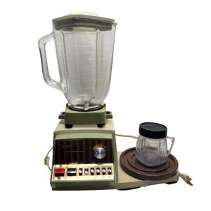 May include: A vintage blender featuring a clear glass jug and a smaller glass jar. The blender has a green base and a control panel with buttons and a dial. The smaller jar sits on a brown circular base.