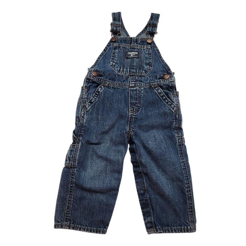 May include: Dark blue denim OshKosh B'gosh overalls. The dungarees have adjustable straps, multiple pockets, and metal hardware. The bib features a small logo patch. The garment is designed for children.