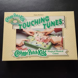 Può includere: Un gioco da tavolo vintage "Touching Tunes" dei Cabbage Patch Kids. La scatola beige presenta testo e grafica verdi e bianchi. Il gioco presenta una base verde con pezzi di puzzle e il testo "Magical Musical Game".