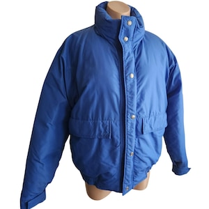 Peut inclure: Une veste matelassée bleu vif dotée d'un col montant, de manches longues avec poignets réglables et d'une patte de boutonnage avant avec des boutons-pression argentés. La veste comprend deux grandes poches avant rectangulaires et un ourlet élastique.