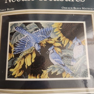 Op de afbeelding: Borduurpatroon met twee blauwe gaaien die op zonnebloemtakken zitten. Het patroon is getiteld "Early Blues" en "Oiseaux Bleus Matinaux".
