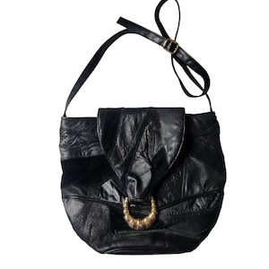 May include: Black leather crossbody bag with a patchwork design. The bag features a flap closure with a gold-toned metal accent. The adjustable strap is black. The bag is a vintage style.