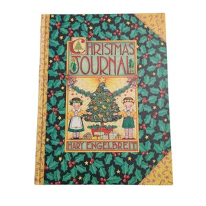 May include: A green and yellow Christmas journal with a holly and candy cane pattern. The cover features a Christmas tree with ornaments and two children standing on either side of the tree. The text on the cover reads "Christmas Journal" and "Mary Engelbreit".