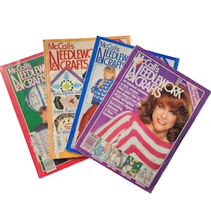 Può includere: Una collezione di quattro riviste vintage McCall's Needlework & Crafts con copertine colorate che mostrano vari progetti artigianali, tra cui maglia, uncinetto e ricamo, con testo che descrive modelli per maglioni, coperte e bambole.