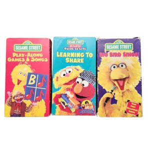 May include: Three Sesame Street VHS tapes with Big Bird and other characters. The tapes are titled "Play-Along Games & Songs", "Learning to Share", and "Big Bird Sings!" The covers are brightly coloured with cartoon illustrations.