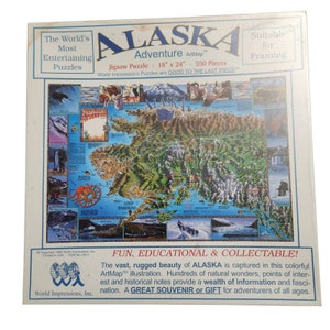 Könnte beinhalten: Ein 550-teiliges Puzzle von Alaska mit einer farbenfrohen Kartenillustration, die Berge, Flüsse und Gletscher zeigt. Das Puzzle ist 45,7 cm x 61 cm groß und Teil der ArtMap-Serie von World Impressions. Die Schachtel zeigt den Text "ALASKA Adventure ArtMap" und "FUN, EDUCATIONAL & COLLECTABLE!"