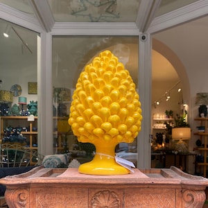 Puede incluir: Una escultura de piña de cerámica amarilla. La escultura está detallada con muchas formas pequeñas y redondeadas y está sentada sobre una mesa de madera.