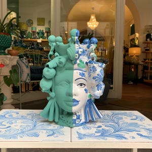 Könnte beinhalten: Eine Keramikskulptur eines Frauenkopfes, halb grün und halb blau-weiß mit floralen Mustern bemalt. Die Skulptur steht auf einem Tisch mit einem blau-weißen Blumenmuster.