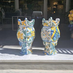 May include: Two large, decorative ceramic urns with intricate floral and geometric patterns in shades of blue, green, yellow, and white. The urns have a crown-like top and a wide base.