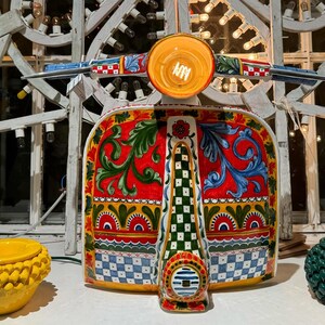 May include: A colorful ceramic scooter with a red, yellow, green, and blue floral design. The scooter has a checkered pattern on the front and a white and blue stripe on the back.