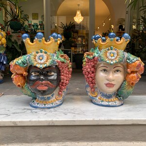 May include: Two ceramic planter heads with colorful floral and fruit designs. The planter on the left has a black face with a mustache and a crown. The planter on the right has a white face with a crown and grapes.