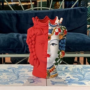 Könnte beinhalten: Eine rote und weiße Keramikvase mit einem Gesichtsdesign. Die Vase ist mit bunten Blumen und geometrischen Mustern verziert.