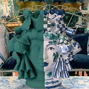 May include: A ceramic vase with a split face design. One side is painted in a teal green color and the other side is painted in white with blue and green floral patterns. The vase is decorated with intricate details and has a unique and whimsical style.