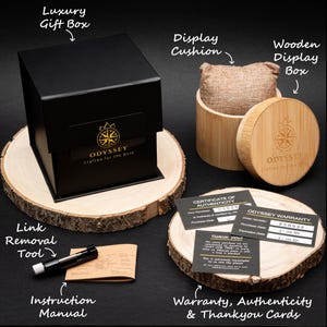 An Image of the watches packing, including a black luxury gift box, wooden display box and cushion, metal link removal tool, and warranty, authenticity and thank you cards.