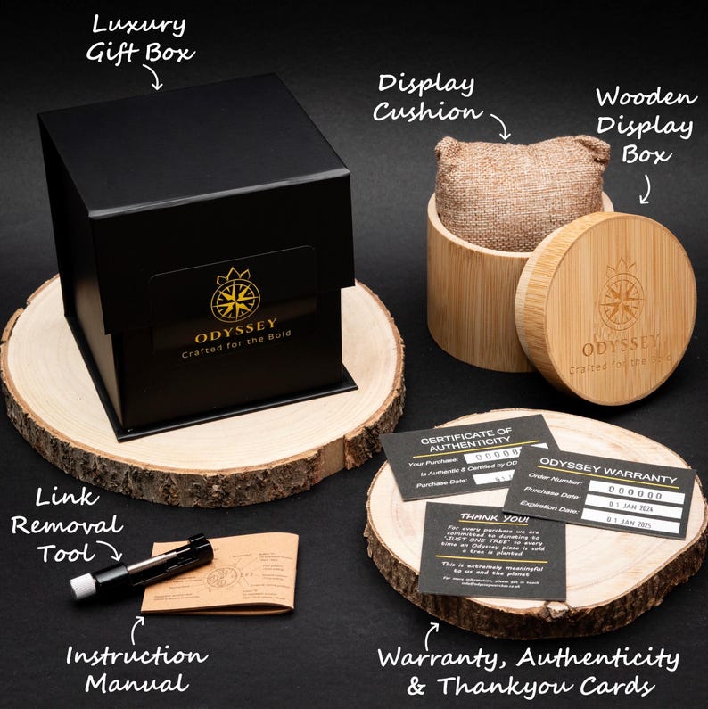 May include: A black gift box with a gold logo that reads "ODYSSEY Crafted for the Bold" sits on a wooden base. The box is surrounded by other packaging materials, including a wooden display box, a display cushion, a link removal tool, an instruction manual, a certificate of authenticity, a warranty card, and a thank you card.