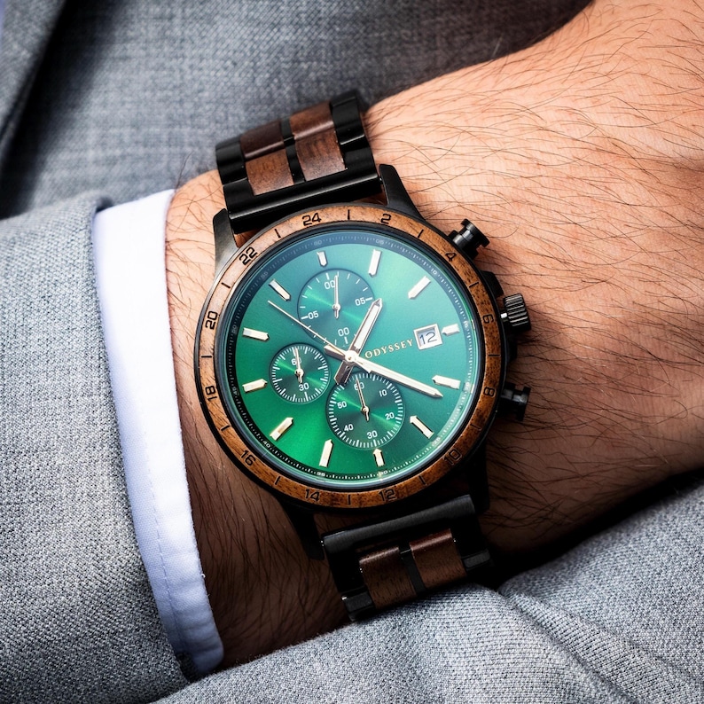 A beautiful wooden watch, with green face surrounded by a walnut bezel accompanied by a walnut and black stainless steel strap. On a mans wrist in a grey suit.