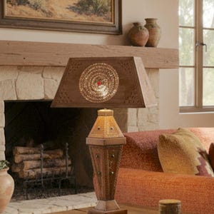 May include: A white ceramic mug with a black handle and the text "But First, Coffee" in a bold, black font. The mug is set against a blurred background, suggesting a cozy setting.