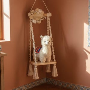 May include: A wooden hanging shelf with a stuffed llama. The shelf is suspended by macrame rope and features a wooden sign that reads "Hello World" and "Family". The llama has a colorful blanket.