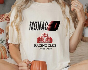 May include: White t-shirt with a black and red graphic design. The graphic features the word "MONACO" with a red racing car and the text "RACING CLUB MONTE CARLO".