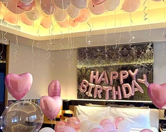 Könnte beinhalten: Ein Raum, der mit rosa und weißen Luftballons für eine Geburtstagsfeier dekoriert ist. Herzförmige Luftballons und ein großes "Happy Birthday"-Luftballonbanner sind zu sehen. Ballons befinden sich auf dem Bett und an der Decke.