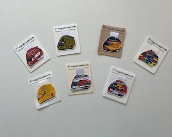 May include: A collection of seven magnetic bookmarks featuring Formula 1 racing helmet designs. Each bookmark has a different helmet design with various colors and patterns, including the text "F1 magnetic bookmarks".