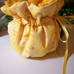 Könnte beinhalten: Ein gelber Teekannenwärmer mit Blumenmuster und gelbem Band.
