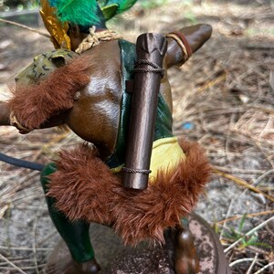 以下が含まれることがあります： フィギュアに緑と黄色の羽根のヘッドドレスとロープのディテールが付いた茶色の木製の矢筒