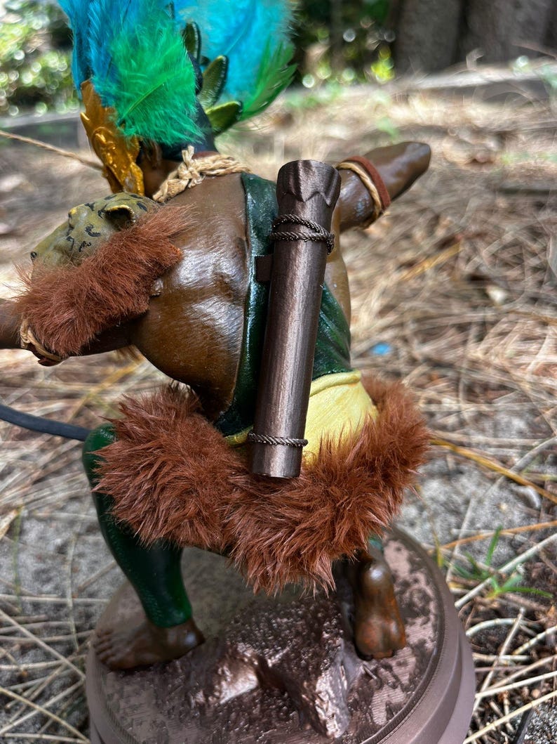 以下が含まれることがあります： フィギュアに緑と黄色の羽根のヘッドドレスとロープのディテールが付いた茶色の木製の矢筒