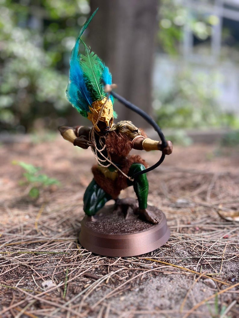 以下が含まれることがあります： 羽根飾りをかぶった人物の緑と茶色の置物で、弓矢を持っています。置物は茶色の台座の上に立っています。