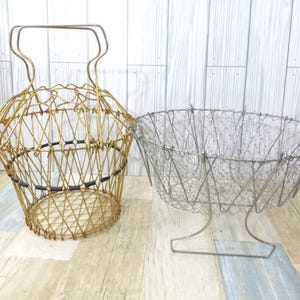 May include: Two wire baskets. One is gold-colored with a handle and a geometric design. The other is silver-colored, oval-shaped, and sits on a wire stand. Both baskets are empty and appear to be vintage.