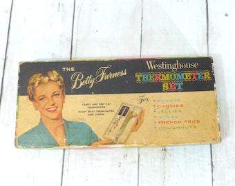 May include: A vintage Westinghouse Thermometer Set box featuring an illustration of Betty Furness. The packaging includes text listing uses for roasts, candies, jellies, icings, french fries, and doughnuts, along with a graphic of the included tools.