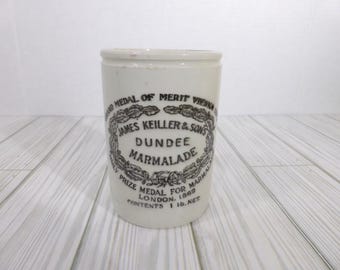 May include: A cylindrical white ceramic marmalade jar featuring black printed text that reads James Keiller & Sons Dundee Marmalade, Grand Medal of Merit Vienna 1873, Prize Medal for Marmalade London 1862, and the net weight contents 1 lb. net.