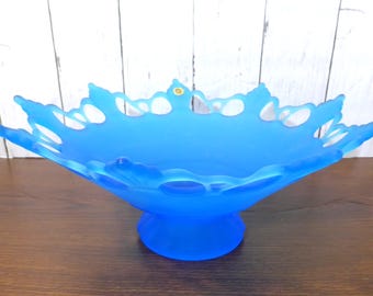 May include: A vibrant blue frosted glass bowl featuring a wide, scalloped, and openwork rim with a pedestal base. The bowl has a smooth, matte finish and a small circular gold-colored sticker near the top edge of the decorative, cutout rim.