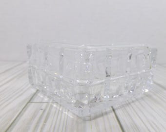 May include: A clear, square glass bowl featuring a geometric grid pattern of raised, textured squares across its exterior surface. The bowl has thick, transparent walls and a structured, faceted design that catches light, creating a repeating pattern.