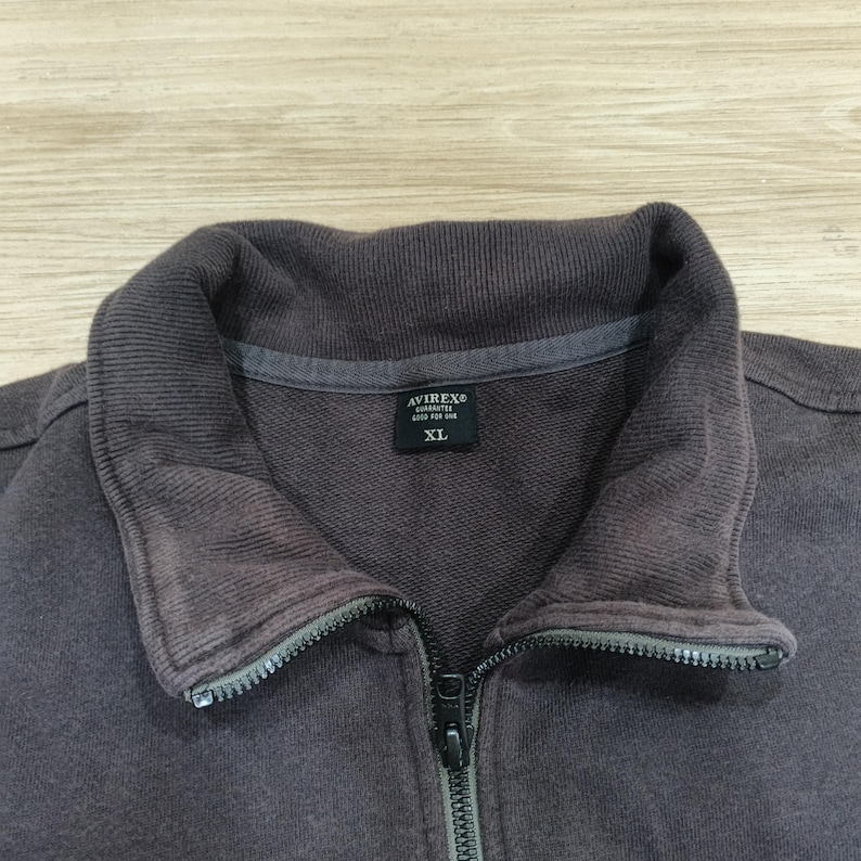 Puede incluir: Primer plano de una sudadera con cremallera marr&oacute;n oscuro. El cuello es de un tono marr&oacute;n m&aacute;s oscuro. La cremallera es negra. La etiqueta dice "AVIREX" y "XL".