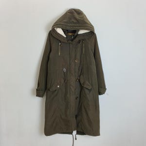 Puede incluir: Parka con capucha verde oliva con cintura ajustable con cordón y múltiples bolsillos. La parka presenta cierre de cremallera y botones, y un cálido forro de piel sintética blanca en el interior de la capucha. Una prenda exterior práctica y elegante.